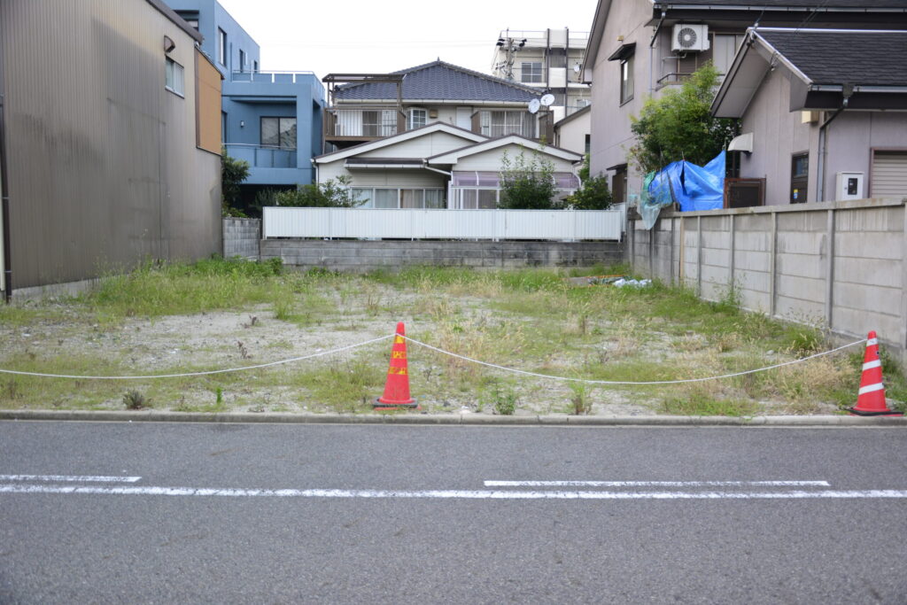 住宅街の中の更地。三角コーンとロープで囲われ、隣家との距離が見える