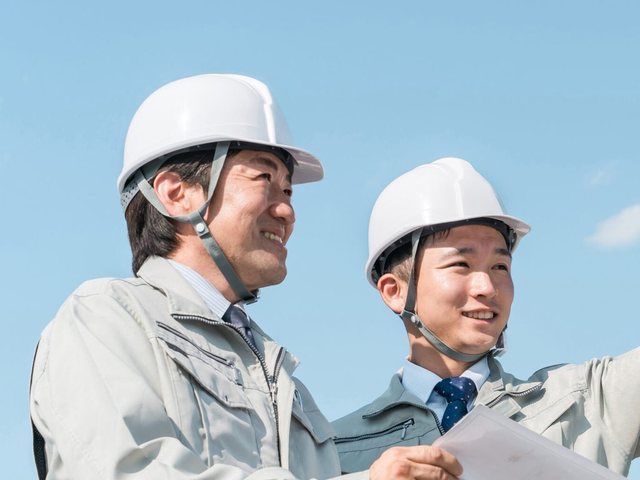 ヘルメットをかぶった現場監督二名が図面を手に打ち合わせている様子