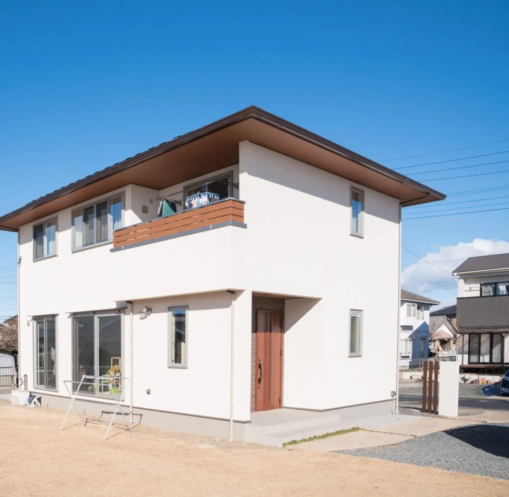 白い塗り壁と、木の手すりが映える二階建て
